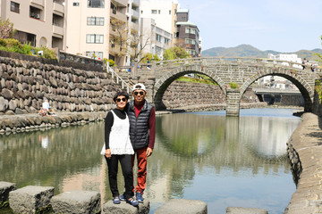 Senior couple posing at Meganebashi Bridge in Nagasaki, Japan. Meganebashi bridge is tourist attraction.