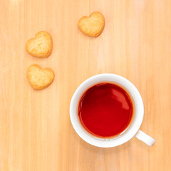 Sweet cookies in shape of heart and cup of tea on wooden table.