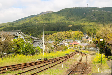 Fototapeta premium Railroad tracks through the village with nature and mountain background in spring season, Yufuin, Japan.