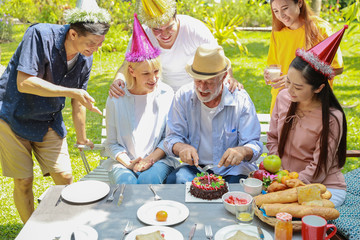 Happy multiethnic family giving surprise gift homemade baked cake to caucasian grandfather on his happy birthday with happy face in backyard outdoor on sunny day