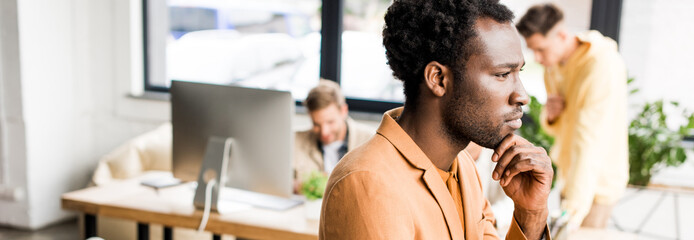panoramic shot of thoughtful african american businessman looking away while standing in office near colleagues