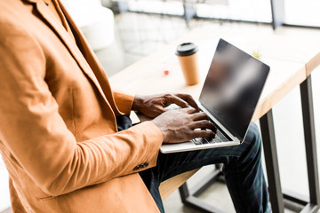 cropped view of african american businessman sitting on desk and using laptop