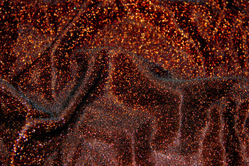 A shiny wavy surface of a brown fabric with orange lurex threads as a background