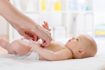 Woman putting diaper on baby on bed in nursery room