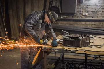 Professional blacksmith sawing metal with hand circular saw at forge, workshop. Handmade,...