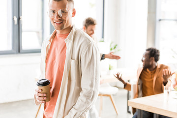 Fototapeta premium young, handsome businessman holding coffee to go and smiling at camera