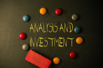 Word writing text Analysis And Investment. Business photo showcasing studying market then do business in large scale Round Flat shape stones with one eraser stick to old chalk black board