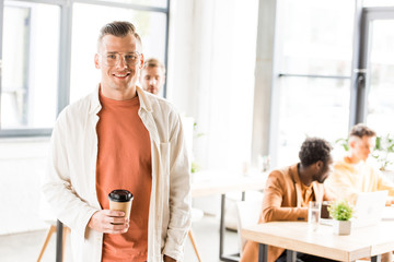 young, handsome businessman holding coffee to go and smiling at camera