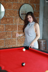full length young beautiful asian woman playing billiards ball on red pool table in club