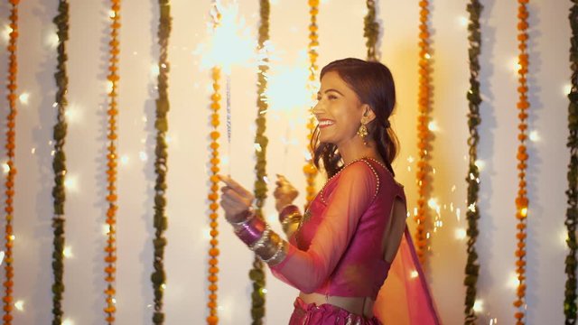 Beautiful young woman having fun with firecrackers in traditional clothing - Diwali festival. Attractive Indian female bursting pencil crackers (phuljhadi) and dancing while celebrating Diwali/Dipa...