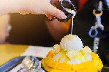 Close up woman's hand pouring Sweetened Condensed Milk on bingsu mango ice cream Korean dessert