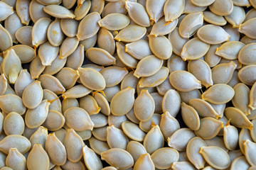 A layer of drying white-gray pumpkin or zucchini seeds extracted from the ripe fruits of vegetables, piled in a heap. Natural or organic background, wallpaper.