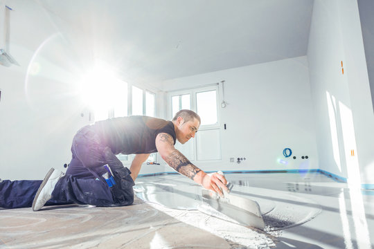 m&auml;nnliche Arbeitskraft, die mit selbstnivellierendem Zementm&ouml;rtel w&auml;hrend der Bodensanierung arbeitet