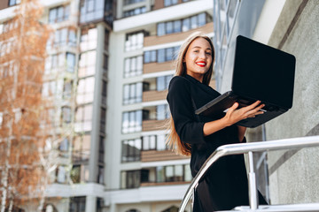 Naklejka na ściany i meble Happy businesswoman holding laptop against city background.- Horizontal image