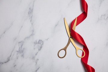 Grand opening background. Gold scissors with red ribbon on a marble background