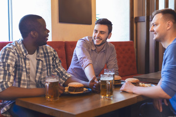 Three young men eating burgers and drinking beer