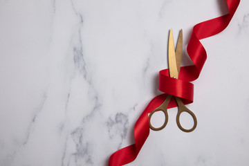Grand opening background. Gold scissors with red ribbon on a marble background