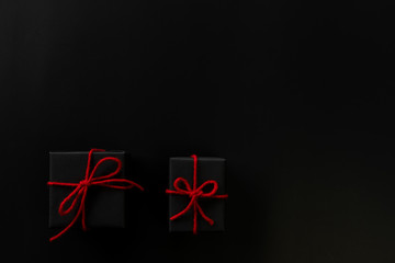 Top view of black christmas gift boxes with red rope bow on black background with copy space for text., black friday advertisement.