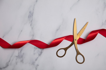 Grand opening background. Gold scissors with red ribbon on a marble background