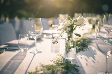 Beautiful outdoor table setting with white flowers for a dinner, wedding reception or other festive event. - obrazy, fototapety, plakaty