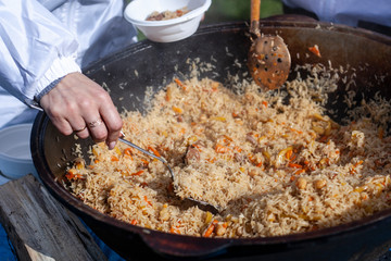 Cook cooks pilaf in a cauldron. Pilaf with vegetables and meat cooked over an open fire. Steam from...