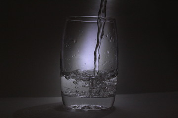 Water falling into the transparent / white glass with black background with some light