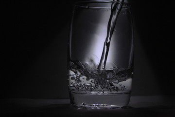 Water falling into the transparent / white glass with black background with some light