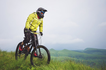 Obraz premium Front view of a man on a mountain bike standing on a rocky terrain and looking down against a gray sky. The concept of a mountain bike and mtb downhill