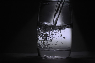 Water falling into the transparent / white glass with black background with some light