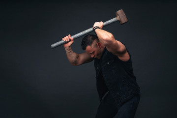 young bodybuilder in black clothes with a sledgehammer in his hands. Studio photography