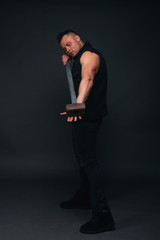 young bodybuilder in black clothes with a sledgehammer in his hands. Studio photography
