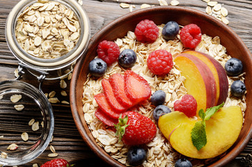 Flat lay of fruit healthy muesli with peaches strawberry almonds and blackberry in clay dish on wooden kitchen table