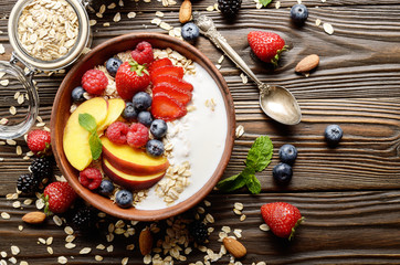 Flat lay of fruit healthy muesli with peaches strawberry almonds and blackberry in clay dish with yogurt