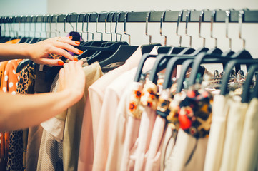 Close up woman hands make choice on colorful clothes on racks in a fashion boutique