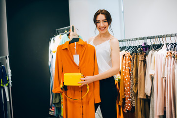 Perfect combinations of dress and bag! Beautiful young woman trying to choose clothes to herself or...