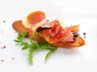 Bruschetta with prosciutto and arugula on a white plate