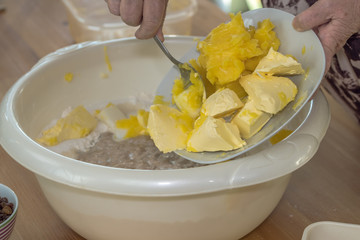 An elderly woman puts butter and clarified butter in a bowl. The dough is then baked to a Christmas stollen. Concept: Christmas and baking