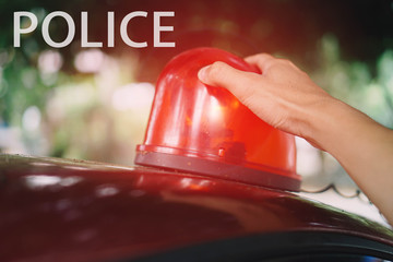 The hand is holding the fire red siren flasher. Siren on police car flashing, close-up.