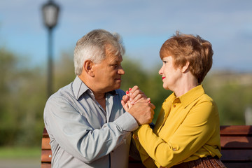 A married couple of pensioners on a bench. Mature lovers hug tightly bench in a city park.