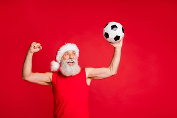 Portrait of crazy santa claus in nicholas hat cap screaming yes raising fists see goal in match wearing sports wear isolated over red background