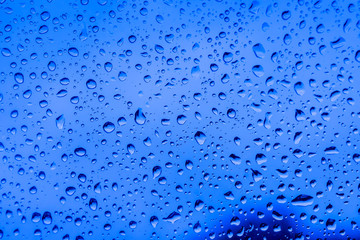 abstract drops on a window glass with blue background close up , rain macro