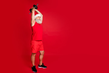 Fototapeta na wymiar Full body photo of concentrated santa claus in hat cap holding dumbbell practice wearing stylish trendy sports wear panties isolated over red background