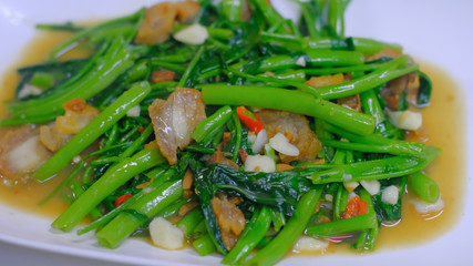 Close up Quick-fried water spinach seasoned with crispy pork spicy chili and soy sauce on white plate, Thai food.
