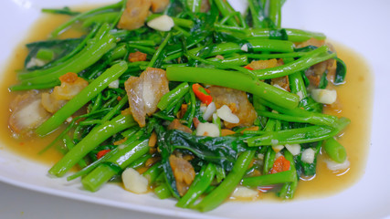Close up Quick-fried water spinach seasoned with crispy pork spicy chili and soy sauce on white plate, Thai food.