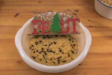 Traditionally prepared Christmas stollen dough lies in a bowl on a wooden table. On a wooden sign is written in German Happy Holidays (Frohes Fest). Concept: Christmas and baking