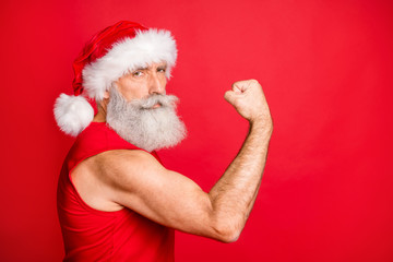 Portrait of confident santa claus show his trainign his triceps wearing trendy sportswear hat cap isolated over red background