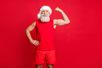 Fototapeta na wymiar Portrait of cheerful santa claus looking smiling showing his biceps wearing red sports wear cap isolated over red background
