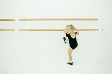 Little ballerina girl in black. Adorable child dancing classical ballet in a white studio. Children...