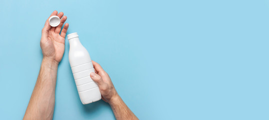 White plastic bottle containers for dairy products in male hands on blue background top view flat lay. Plastic Kefir Yogurt Milk Bottle. Packaging template mockup. Layout for your design