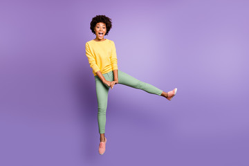 Fototapeta na wymiar Full size photo of cheerful funny funky teen afro american girl jump have fun on autumn weekends spring free time wear yellow pullover green pants trousers isolated over purple violet color background